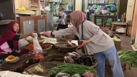 a woman wearing a hijab is buying organic spices sold by a vegetable trader at a traditional market.