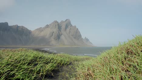 el majestuoso monte vestrahorn en islandia rodeado de una playa de arena como se ve desde una colina de hierba cercana