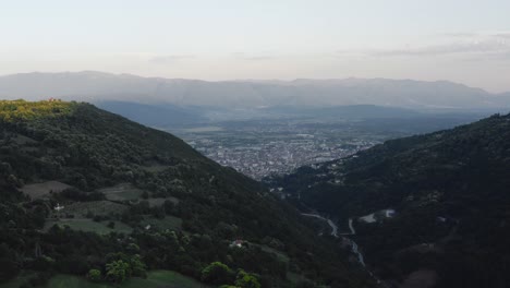 Aerial-view-of-a-beautiful-valley-which-leads-to-scenic-city-with-mountains-in-the-distance