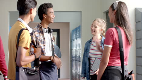 teenagers in high school hallway talking and laughing near lockers, holding books