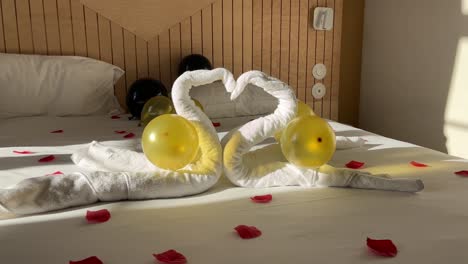 zoom in on a romantic hotel bed with rose petals, swans made from towels and balloons