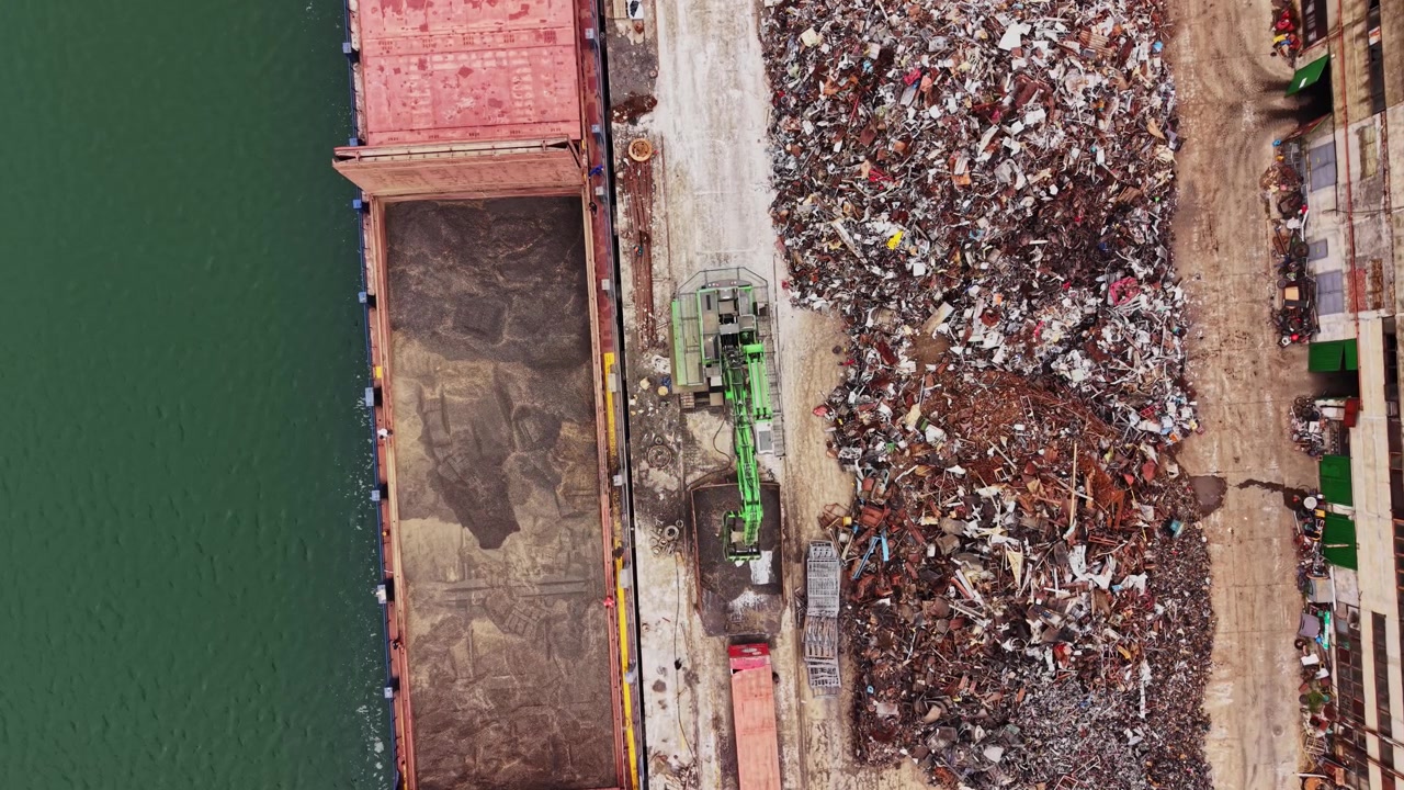 Nave da carico che scarica rottami metallici vicino alla riva in un porto trafficato