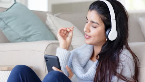 relaxing at home, woman enjoying music on headphones using smartphone