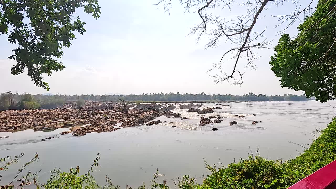 A tranquil river scene with flowing water, surrounded by lush trees and rocks under bright daylight