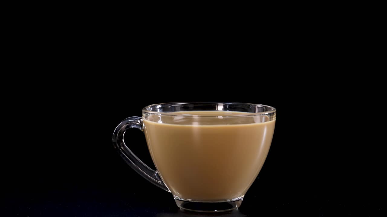 A sugar cube drops into a glass cup of tea, creating a dramatic splash against a black background