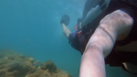 a tourist on vacation scuba diving holding a gopro towards themselves as they swim through crystal clear blue water of maracajau in rio grande do norte, brazil