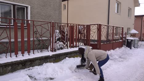 Junges-Asiatisches-Mädchen-In-Winterkleidung,-Das-Schnee-In-Der-Einfahrt-Des-Hauses-Schaufelt