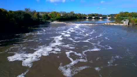 drone flying over white river with bridge in background, indianapolis