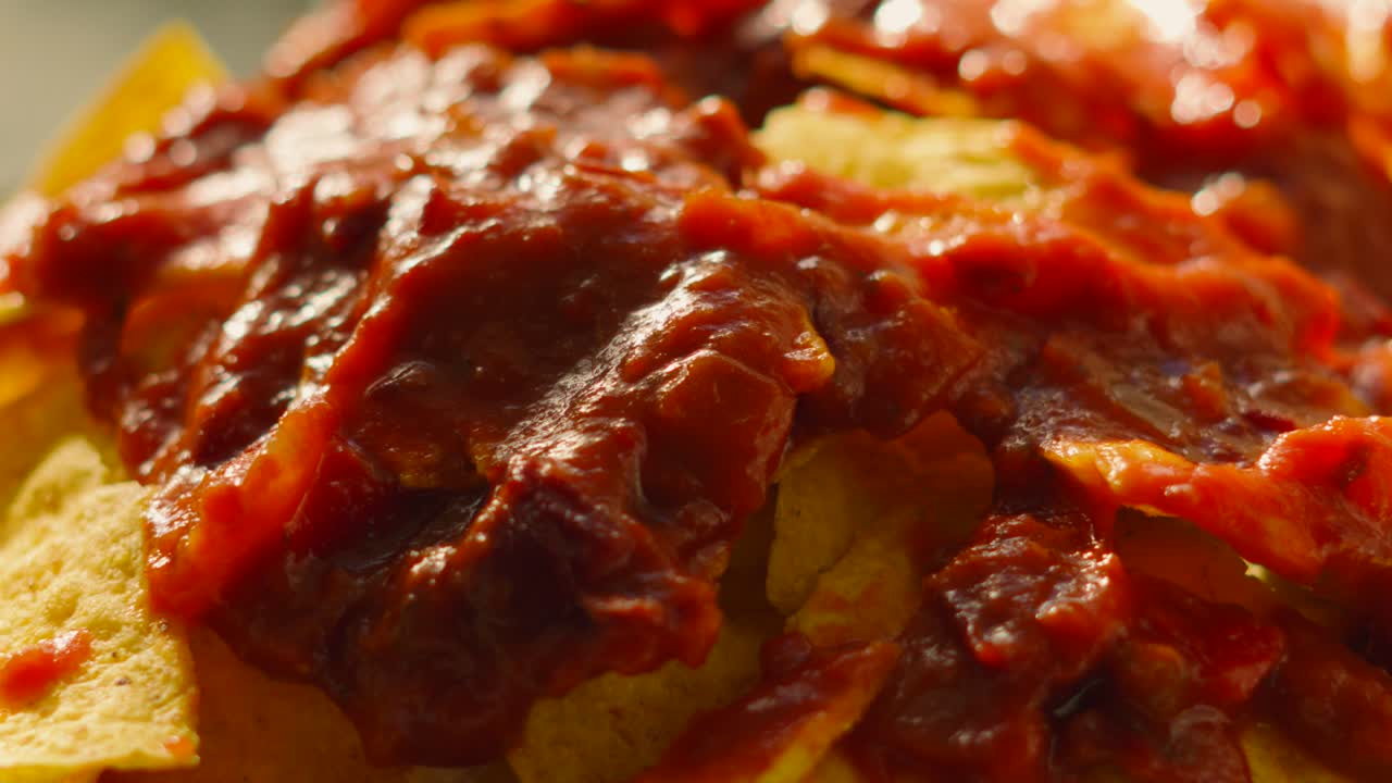 Slow Moving Shot Across Bean Salsa on Top of Crispy Tortilla Nacho Chips Ready to be Loaded with Cheese. Tex-Mex Mexican Party Snack