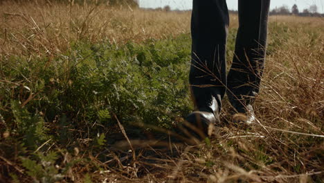 Shot-of-young-mans-legs,-wearing-dress-shoes-and-a-suit-walking-on-the-farm-field-in-late-autumn,-clear-blue-sky,-trees-in-the-distance