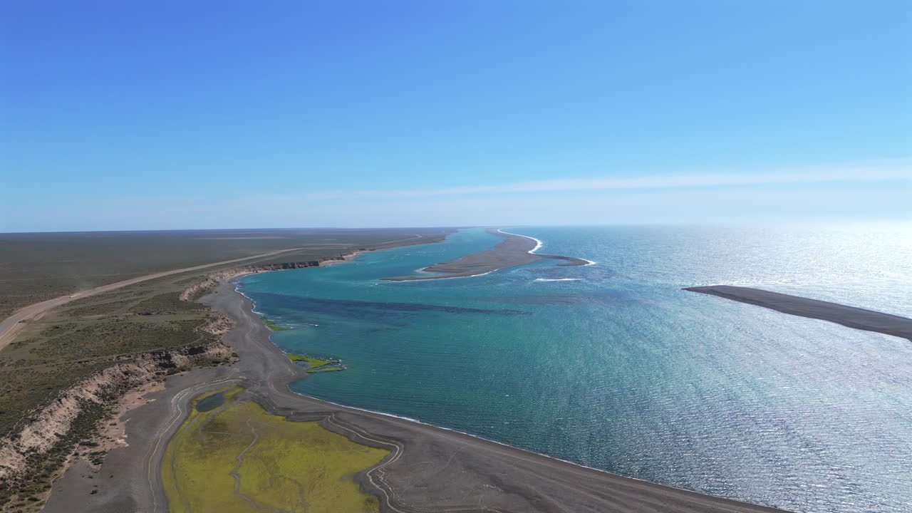 Aerial view of a curving coastline with calm blue waters and wetlands, Peninsula Valdes, Argentina.