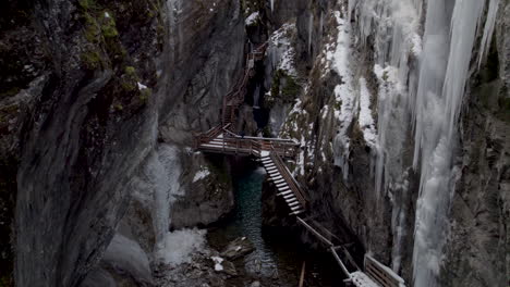 drone tilting up in austria at sigmund thun klamm between two cliffs in the woods with icicles on both walls with stairs leading up between the cliffs