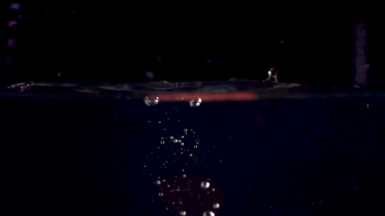 high speed camera slow motion reverse video of a red tomato slice splashing into water. Black background