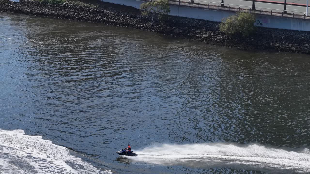 A jet ski speeds across Gold Coast waters, creating dynamic waves under bright daylight. Captured from an aerial perspective