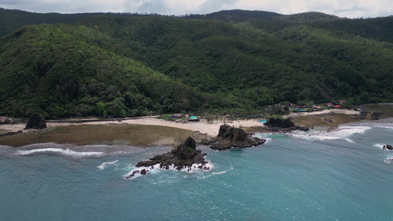 A sweeping drone shot captures the lush green mountain beside the shore, with a winding coastal road offering a stunning ocean view.
