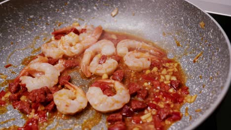 top view of shrimps being fried with chorizo garlic and diced onion along with oil in a pan in the kitchen