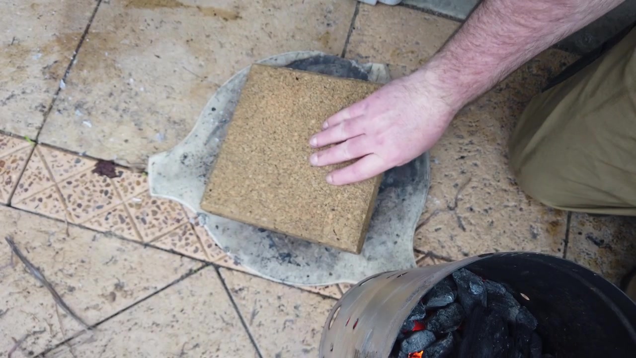 Persona che indossa guanti protettivi spegne con attenzione bricchette di carbone ardenti con un coperchio di sughero per conservarle per un uso successivo in un barbecue.
