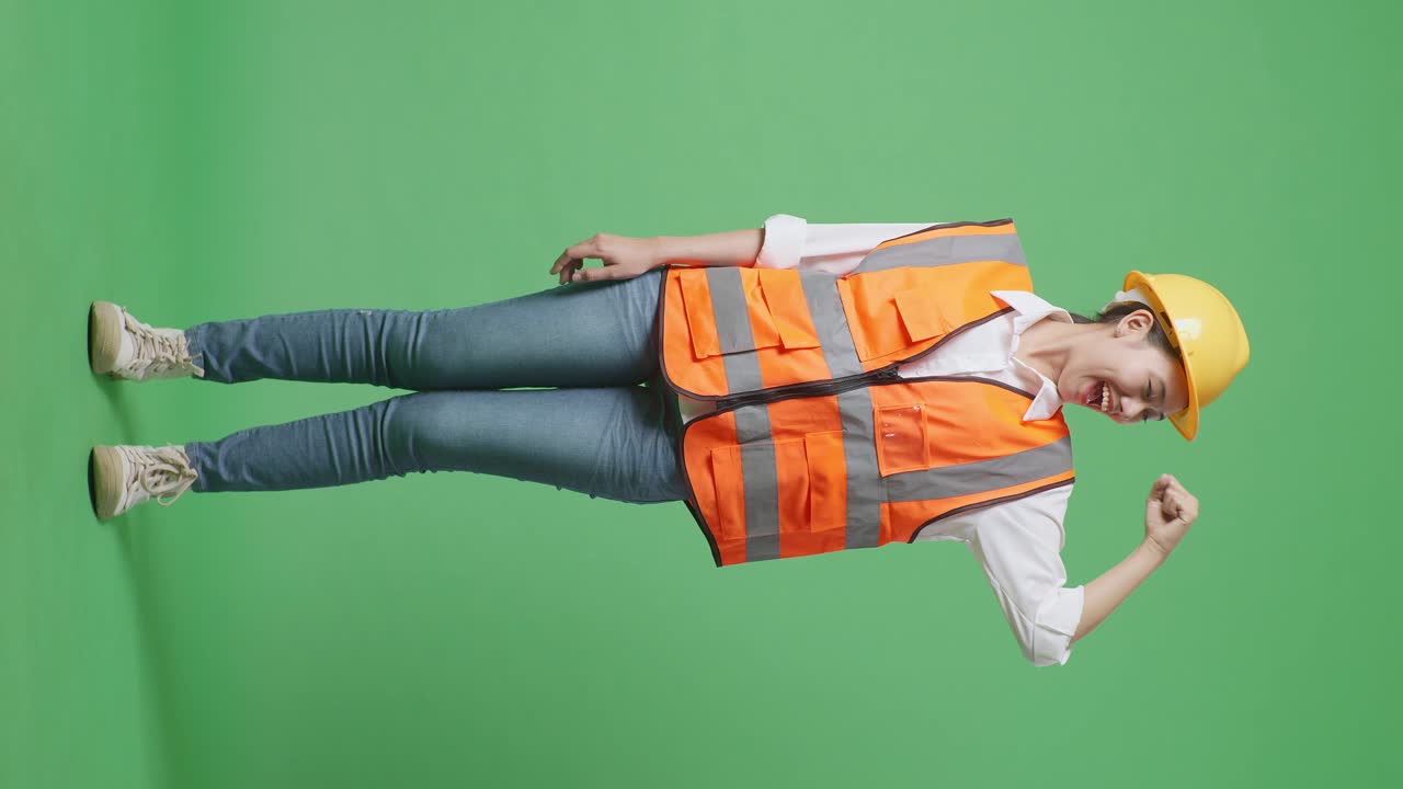 안전 헬을 입은 아시아 여성 엔지니어의 몸이 가득 차 있으며, 녹색 스크린 배경 스튜디오에 서서 카메라에 미소 짓고 있습니다.