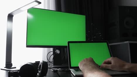 el programador masculino está trabajando en una computadora portátil con dos monitores con pantallas verdes de clave de croma en una oficina moderna. el freelance está usando la computadora en el escritorio en el lugar de trabajo, escribiendo algoritmos, mensajes en el teclado
