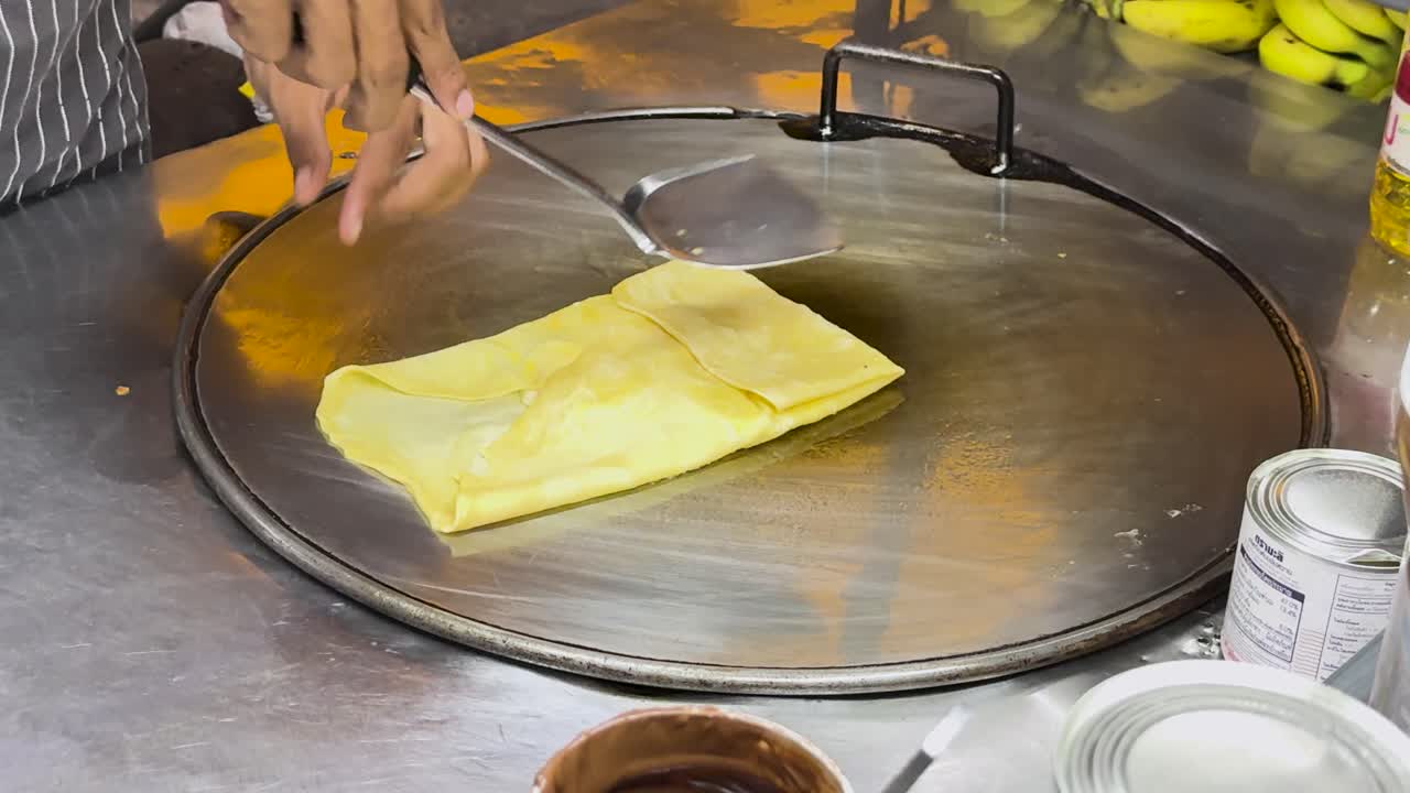 un vendedor callejero prepara hábilmente roti tailandés en una parrilla caliente en phuket, tailandia, mostrando técnicas tradicionales de comida callejera