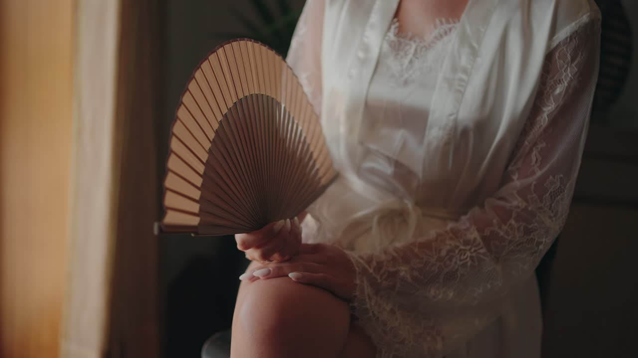 Elegant hold of bamboo fan amid sheer lace sleeves for bridal serenity