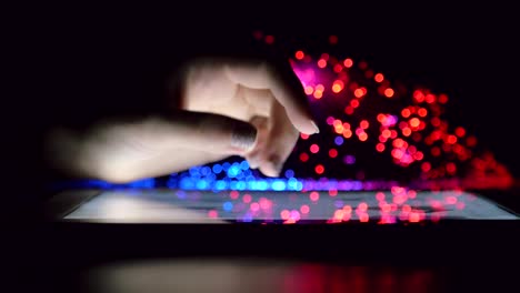 woman hand touching and browsing on tablet device in dark room with colorful blurry fiber optic lights closeup steady shot