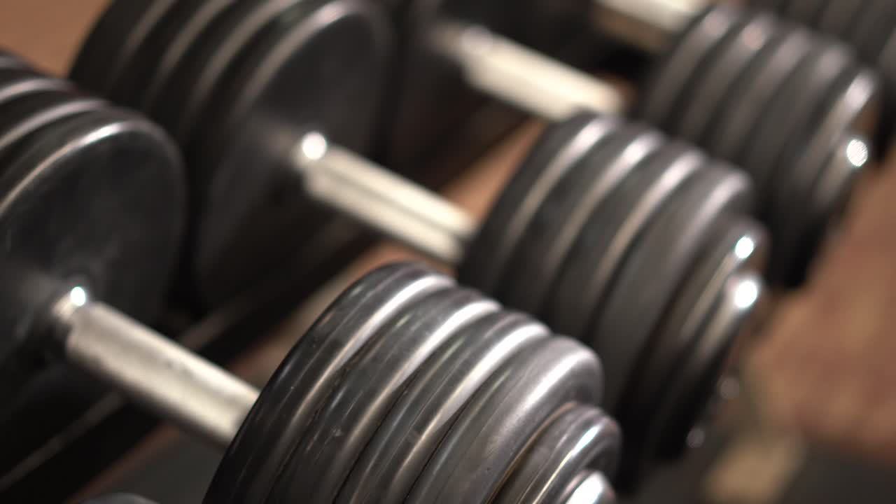 Close-up trage slider-opname naar rechts, neerkijkend onder een scherpe hoek op een rij dumbbells op een rek met geringe scherptediepte