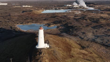 white lighthouse on hill surrounded by volcanic landscape and geothermal pools