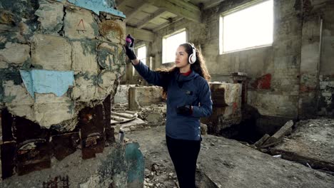 una joven artista de graffiti está pintando con pintura en aerosol dentro de un viejo almacén y escuchando música a través de auriculares inalámbricos. concepto de subcultura juvenil.