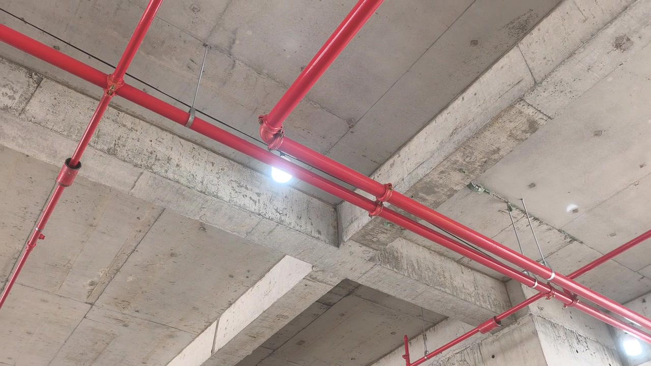 Operai installano una rete di tubazioni antincendio sprinkler in un cantiere edile. Realizzato secondo precisi progetti ingegneristici, questo sistema vitale eroga acqua per sopprimere gli incendi iniziali prima dell'arrivo dei vigili del fuoco