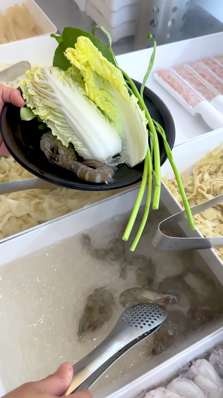 人が金属製のトングを使い、鍋料理用に新鮮な生エビをつまんでいる。