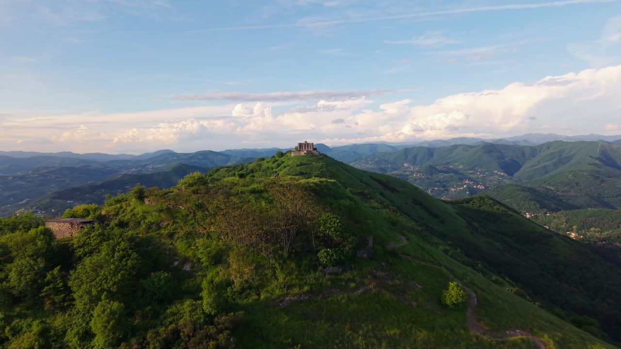 Antico forte su una montagna in Italia con rigogliosa vegetazione circostante e colline distanti.