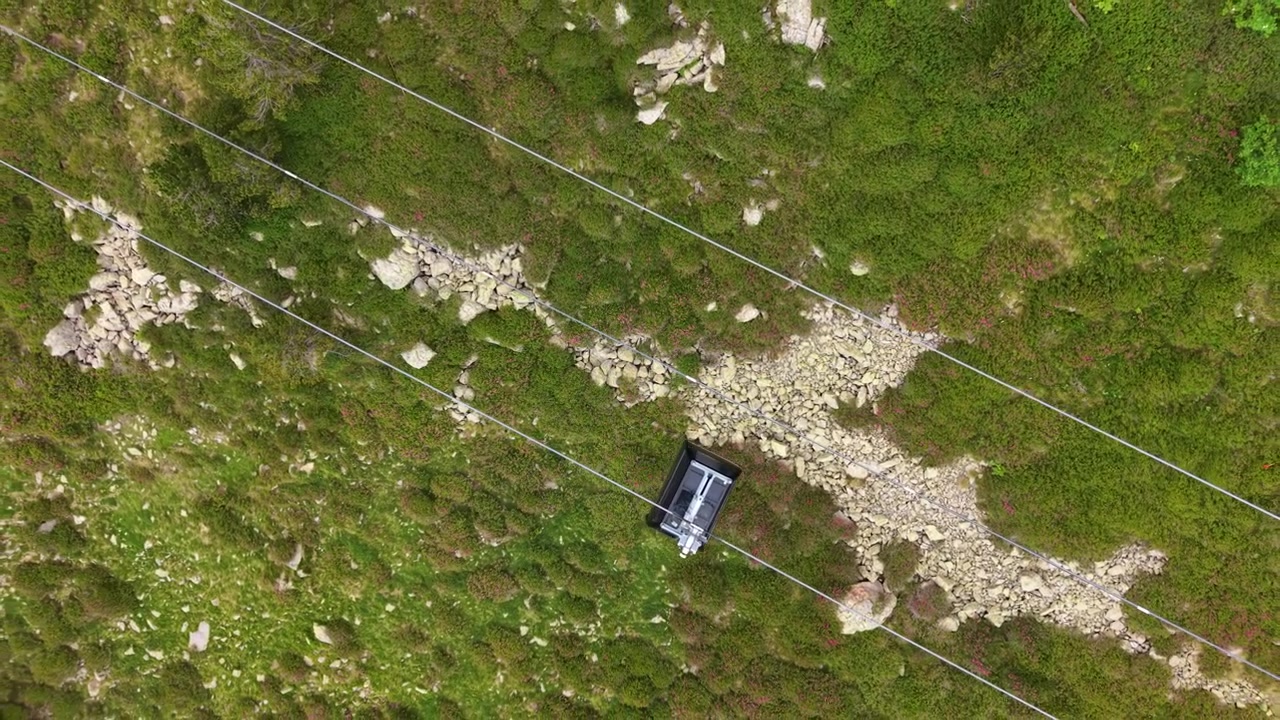 Vista dall'alto di una cabina della funivia sospesa su cavi che attraversa un ripido pendio montano roccioso e verde in Andorra, circondata da muschio e massi sparsi