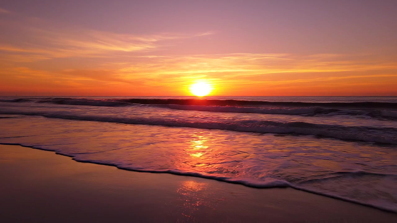 Vibrant orange sunset over calm ocean waves on sandy beach