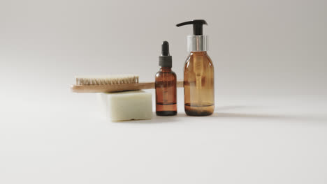 Close-up-of-glass-bottles-with-pumps,-soap,-brush-and-copy-space-on-white-background