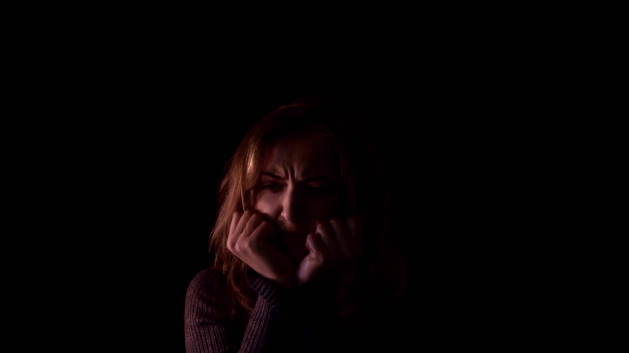 Young woman suffers from anxiety. She is terrified, lonely and shattered. The woman has depression and headache symptoms. It is illuminated by a flashing alarm light