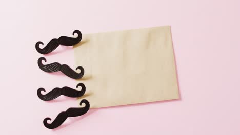 video de cuatro bigotes falsos negros y un sobre amarillo con espacio de copia en un fondo rosa