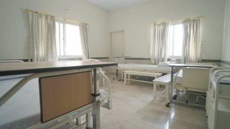 a vacant hospital room showing beds, chairs, and sunlight shining through windows.