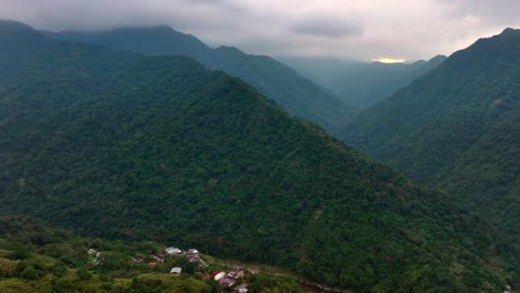 vista aérea de la montaña verde que crece durante un día nublado con un pequeño pueblo en el valle de wulai 烏來??