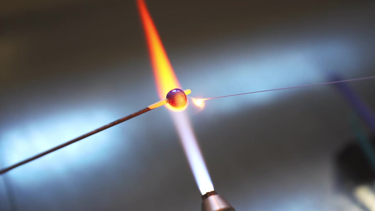 Macro shot of a craftsman melting glass over a torch flame to create traditional Viking beads. Authentic jewelry-making workshop experience in the Lofoten Islands, Norway