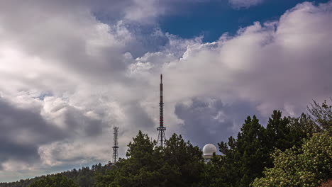 Low-angle-shot-of-radar-antenna-on-top-of-a-mountain-with-white-clouds-passing-by-in-timelapse-at-daytime