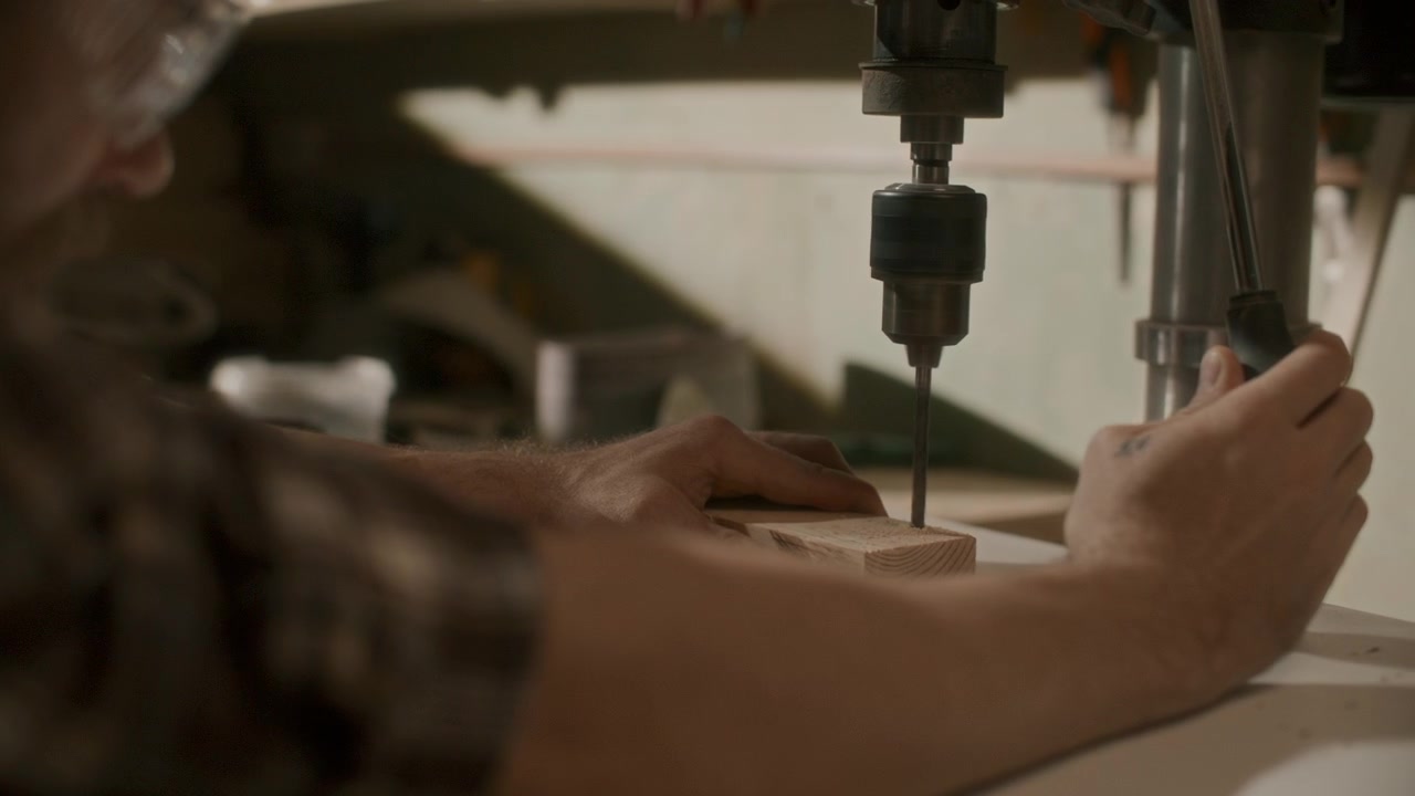 Woodworker Operating Drill Press on Wooden Block in Workshop