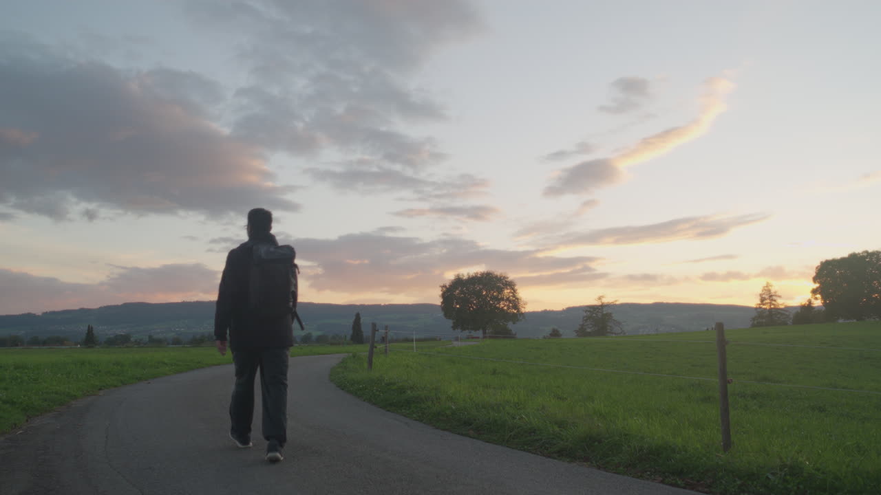 Pria muda dengan ransel mendaki saat matahari terbenam di akhir musim panas, Swiss.