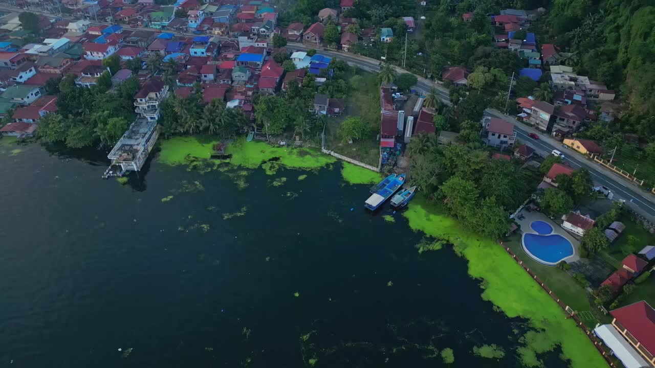 A pull-out aerial of Talisay town with colorful rooftops lining the forested shore of Taal Lake in Batangas, Philippines