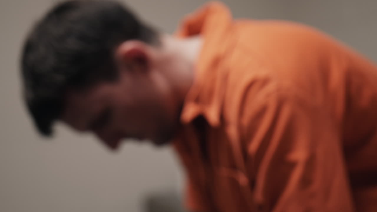 슬프고, 불행하고, 우울하고, 매력적이고, 잘생긴 남자, 범죄 죄수, 오렌지색 정복을 입은 수감자가 감옥에 앉아 있습니다.