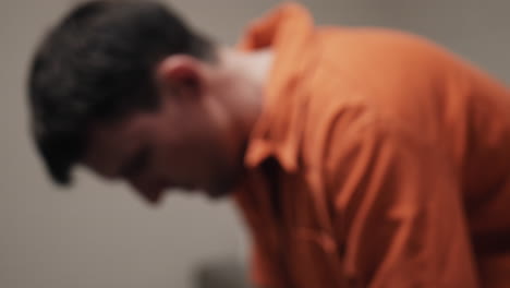 un hombre triste, infeliz, deprimido atractivo, guapo, prisionero criminal, preso en mono naranja sentado en una celda de prisión
