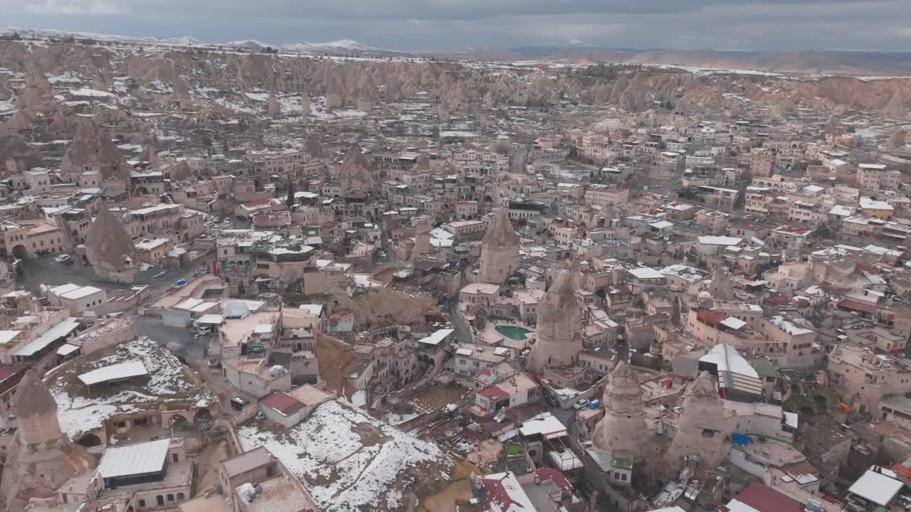 Veduta aerea di Goreme in Cappadocia, Turchia, che mostra abitazioni rupestri, formazioni rocciose erose e tetti innevati attraverso la città storica in inverno.