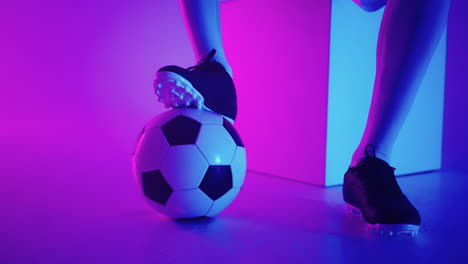 close-up of the foot of a professional black football player standing on the ball in slow motion in the blue-red neon light of the studio. brazilian football player foot on the ball to pose