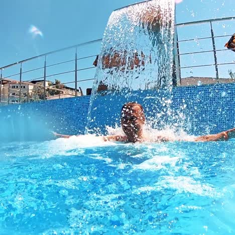 happy man enjoys time in the swimming pool. joyful man standing under the artificial waterfall in the pool in a sunny summer day.
