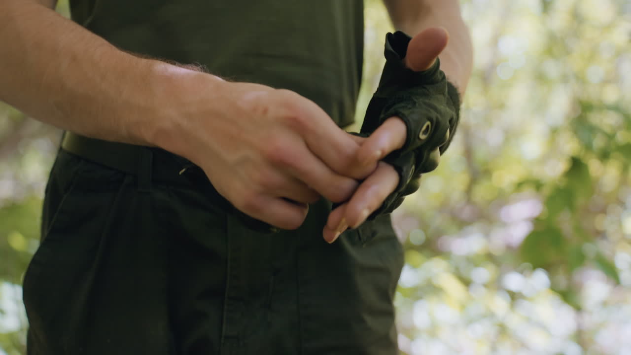 Close up view of tourist removing fingerless glove, veins visible on hand and forearm, belt and cargo pants visible, dappled sunlight filtering through forest canopy casting highlights on skin